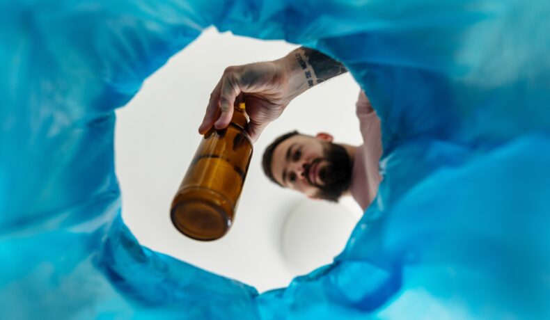 Mężczyzna wrzucający pustą butelkę po alkoholu do kosza – symboliczny gest zerwania z nałogiem i rozpoczęcia regeneracji organizmu